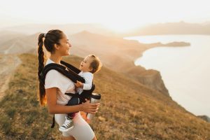 Happy young woman travel and hike with toddler baby in sling. Active lifestyle